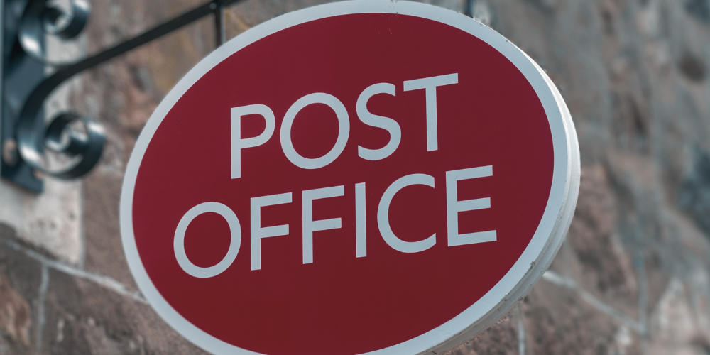 a photo of a sign hanging off a brick wall depicting the logo for the post office